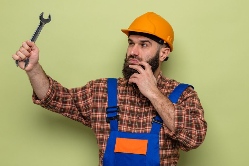 A worker contemplates the wrench he is holding.