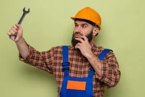 A worker contemplates the wrench he is holding.