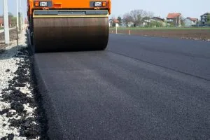 A roller flattens fresh asphalt