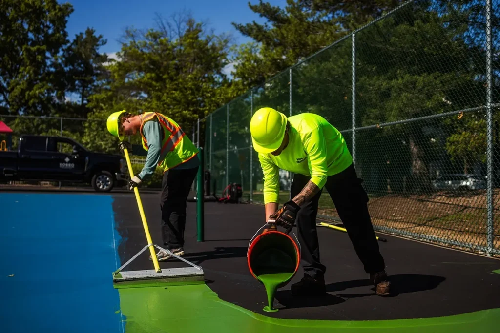 NPP workers pour a new green court surfacing over a tennis court.