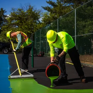 NPP workers pour a new green court surfacing over a tennis court.